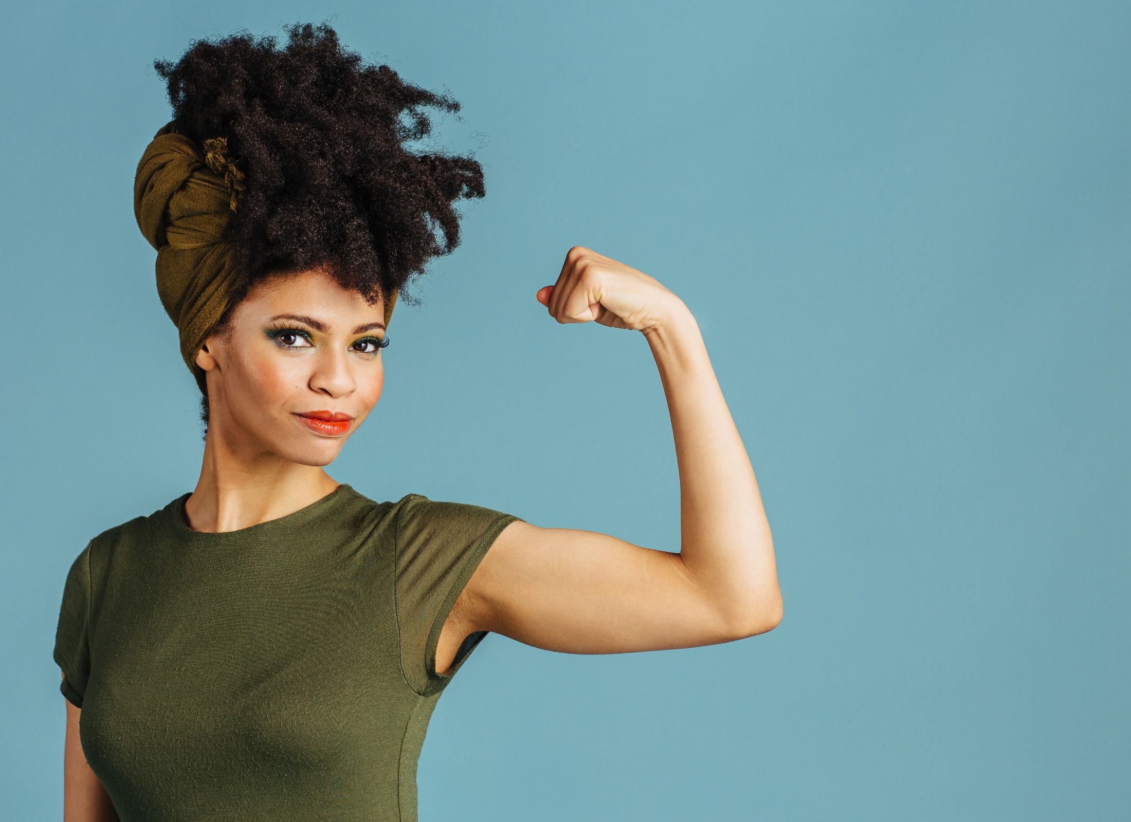 Confident woman flexing arm against blue background.